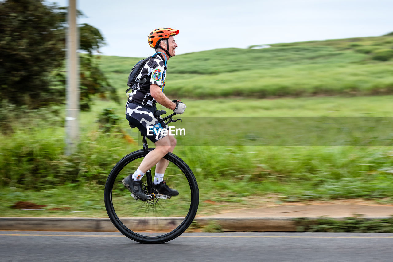 MAN RIDING BICYCLE ON ROAD AGAINST PLANTS