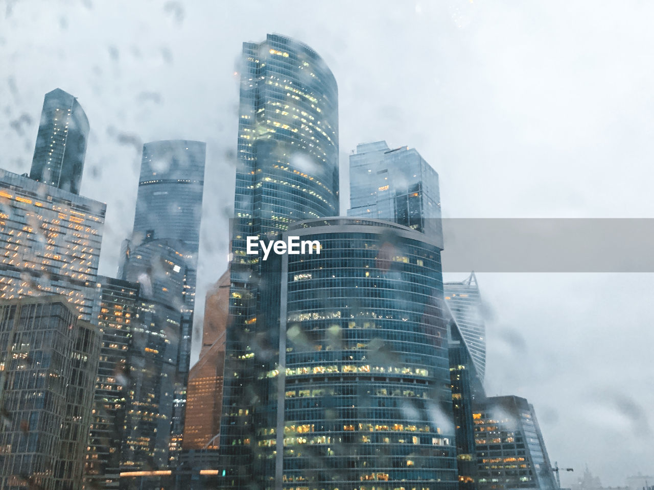 Low angle view of modern buildings in city against sky through glass