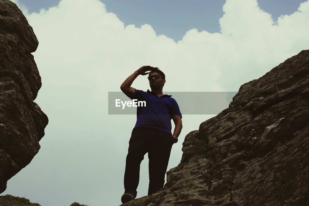 Low angle view of young man standing on cliff against sky