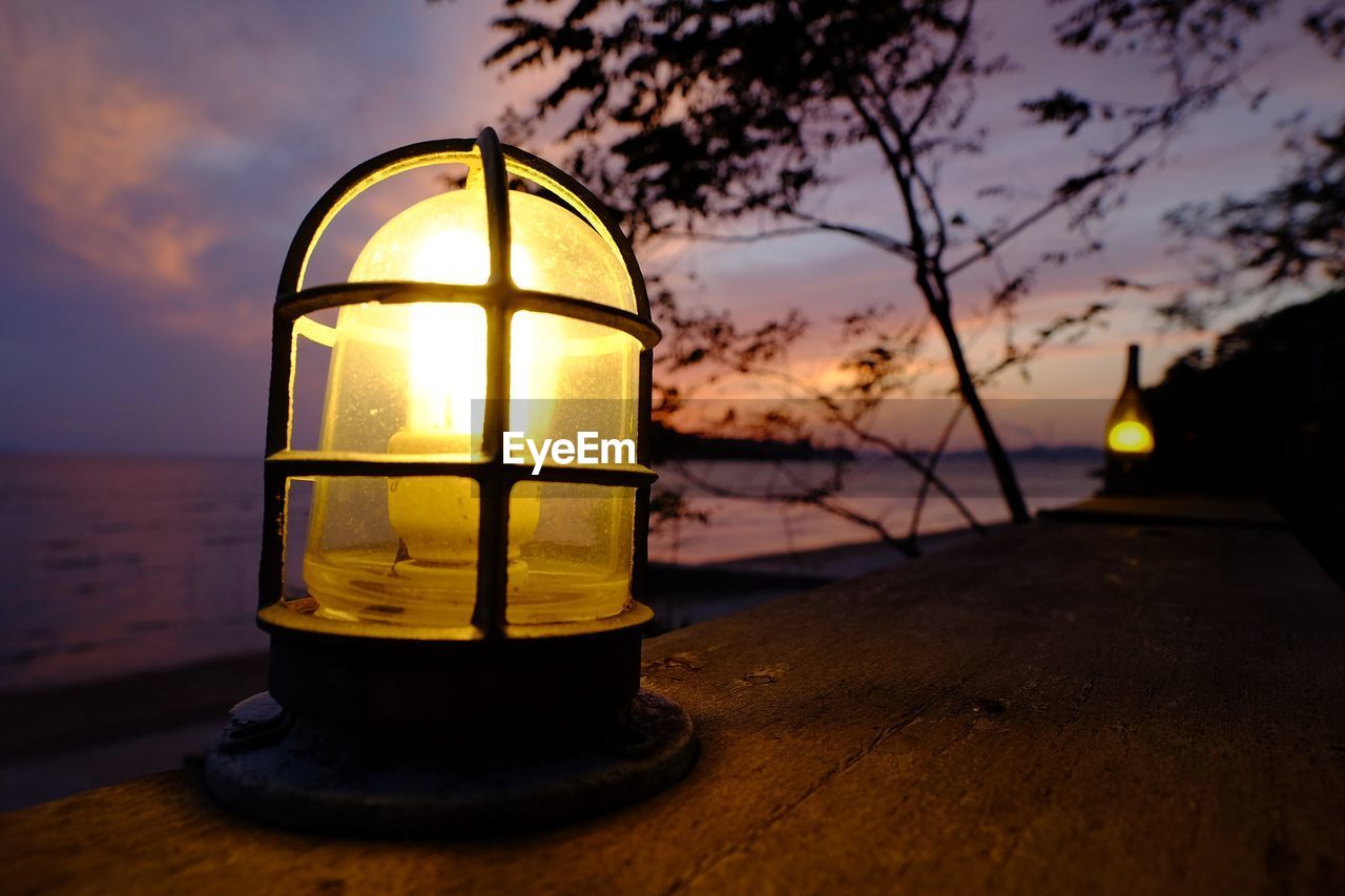 CLOSE-UP OF ILLUMINATED LAMP IN SEA AGAINST SKY