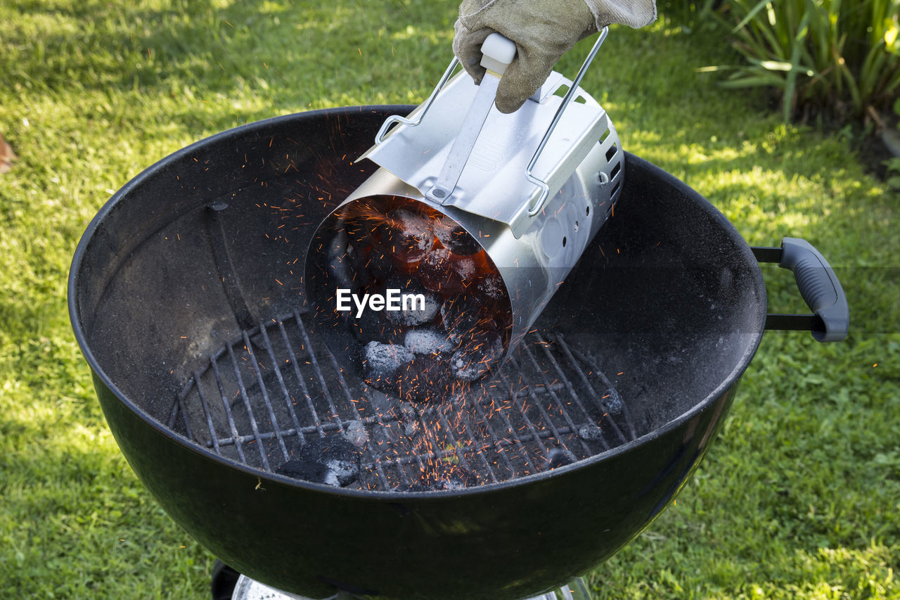 Cropped hand of person pouring coals in barbecue grill on field