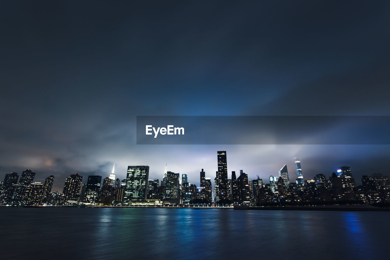 Illuminated modern buildings in city against sky at night