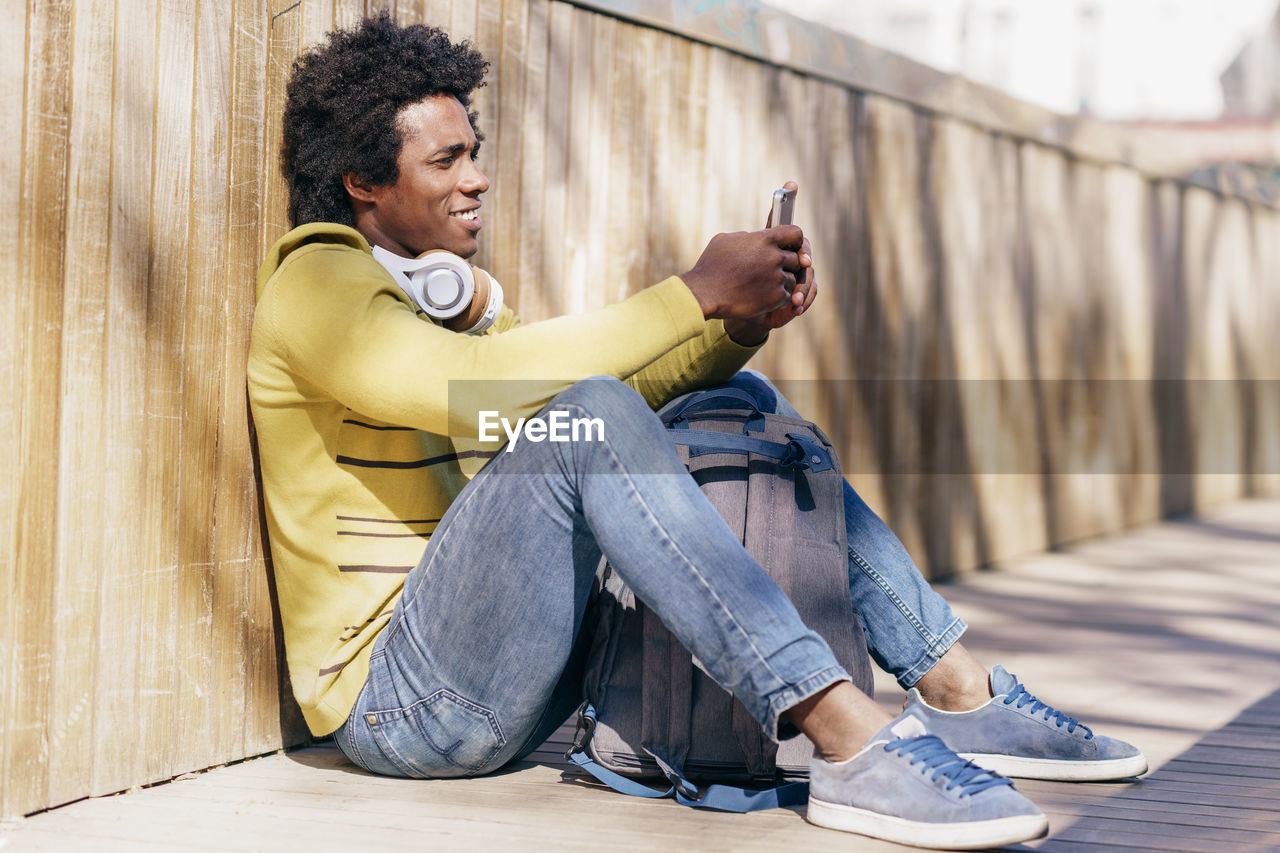 Full length of man sitting on floor while using smart phone outdoors