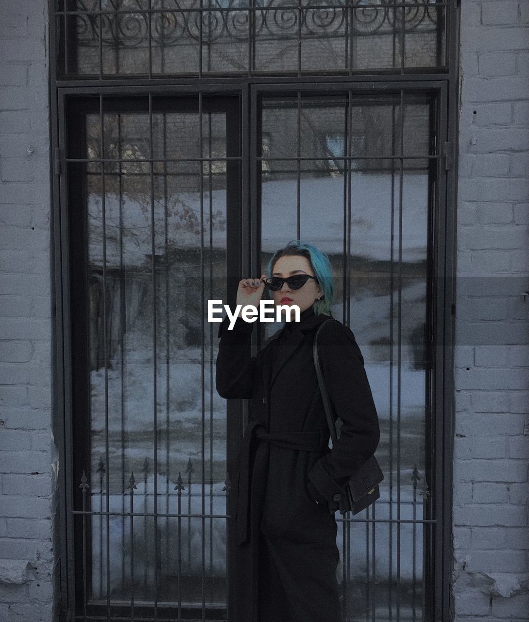 Young woman wearing sunglasses standing against window