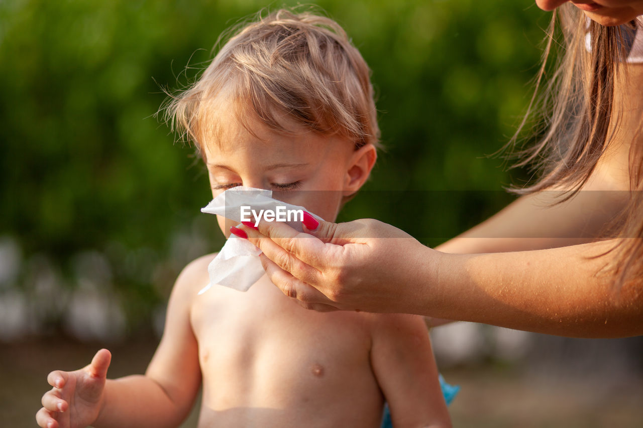 Cropped hand of mother wiping mouth of son 