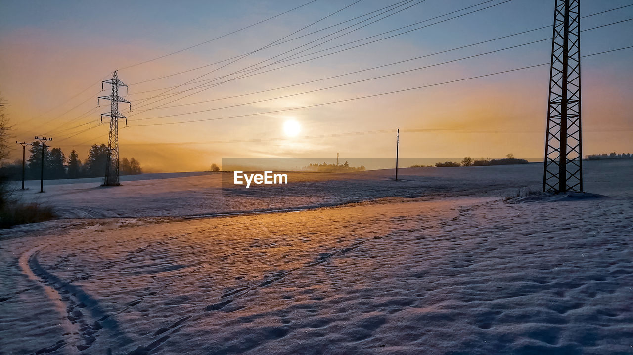 Electricity pylons on land against sky during sunset