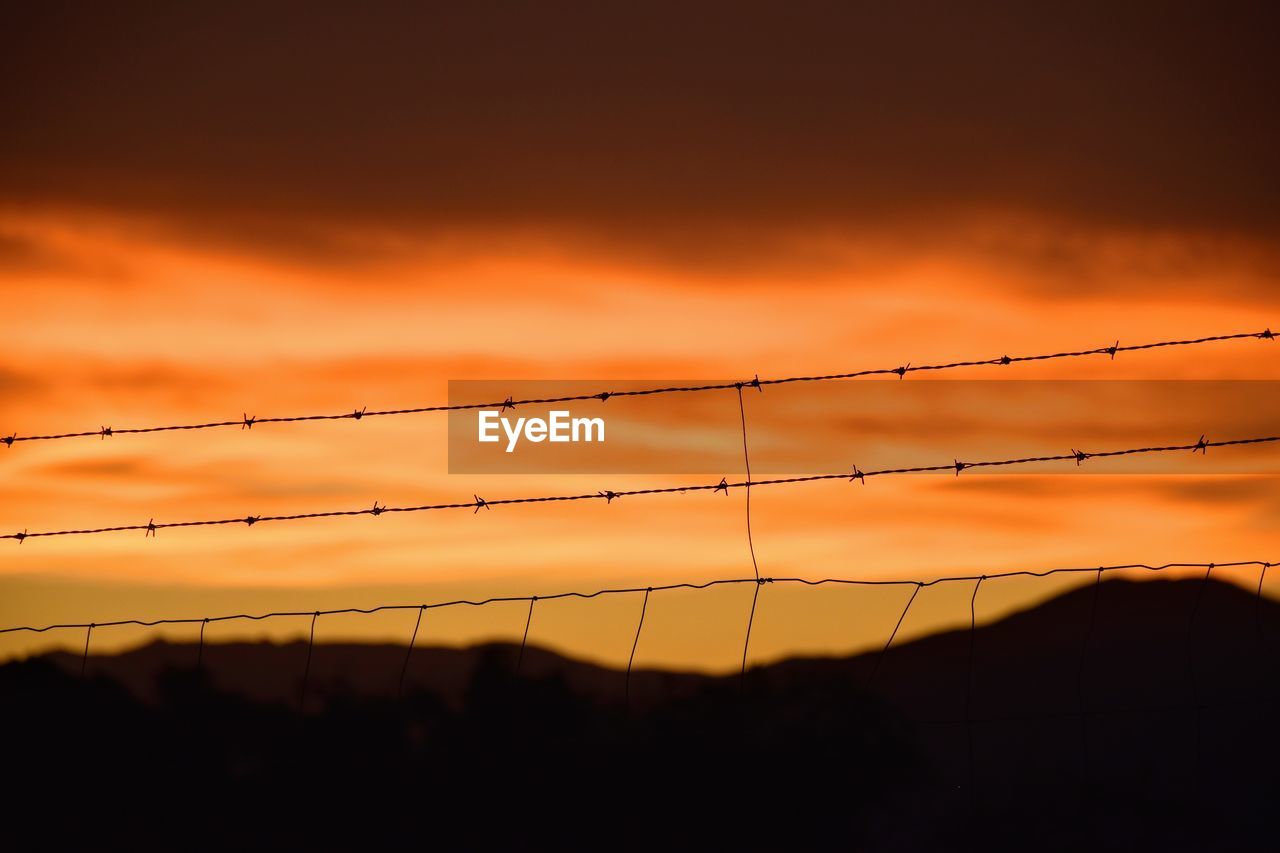 Silhouette barbed wire fence against sky during sunset