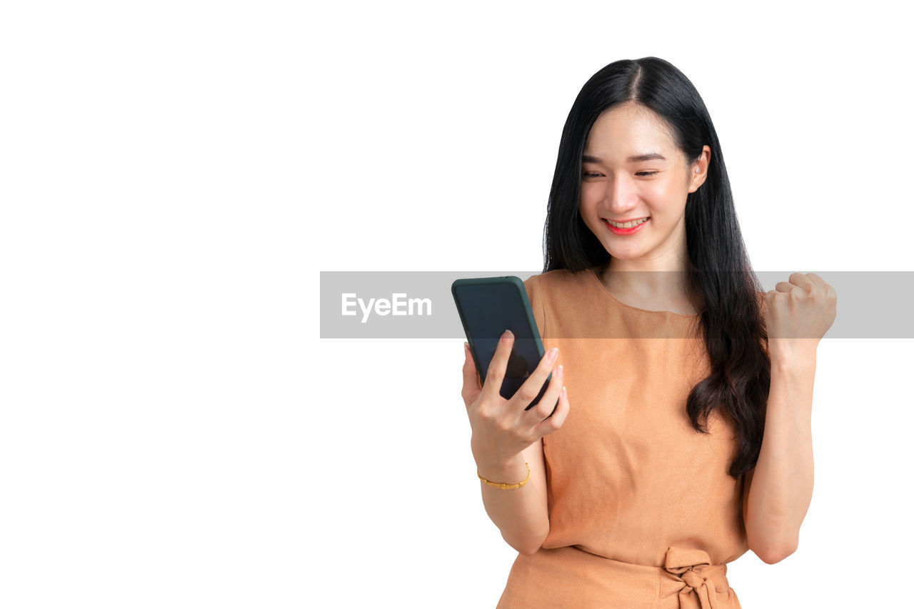 wireless technology, technology, communication, women, one person, finger, adult, smiling, white background, hand, happiness, studio shot, young adult, cut out, copy space, mobile phone, portable information device, smartphone, portrait, arm, cheerful, indoors, front view, emotion, telephone, internet, clothing, long hair, portability, female, waist up, holding, lifestyles, looking, smile, hairstyle, positive emotion, teeth, standing, computer network, human face, person, relaxation, screen, fashion, touch screen, casual clothing, computer, looking at camera, limb, photo shoot, enjoyment, mobile app, using phone, e-mail, cute, activity, digital tablet, showing, business