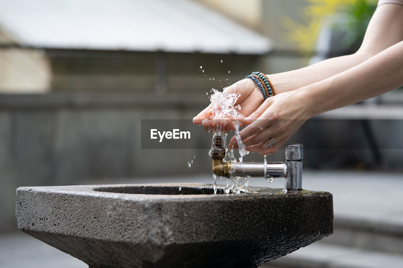 Hands with water pouring from tap in street. drops of water streaming up on fingers of young girl.