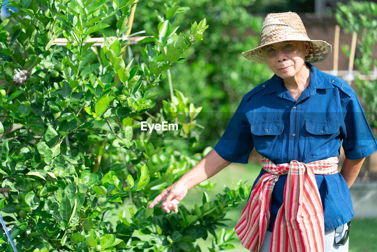 Senior man wearing hat standing by plants outdoors