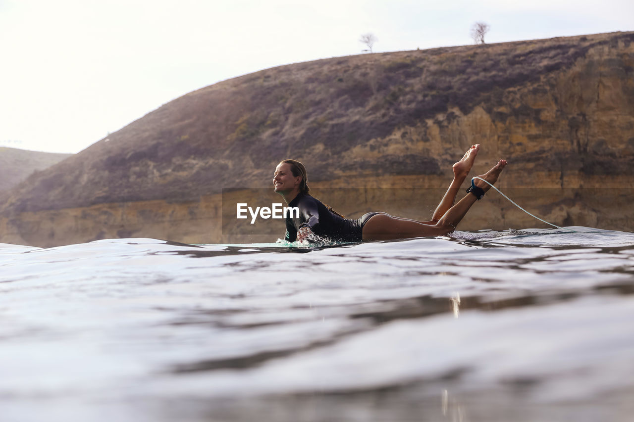 Happy woman sitting on surfboard in sea