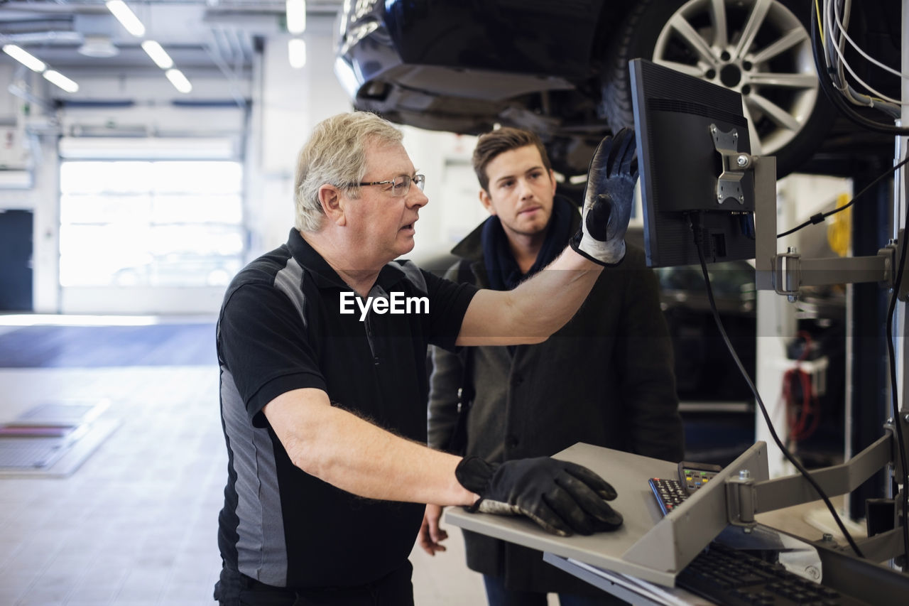 Senior mechanic showing computer monitor while discussing with customer at repair shop
