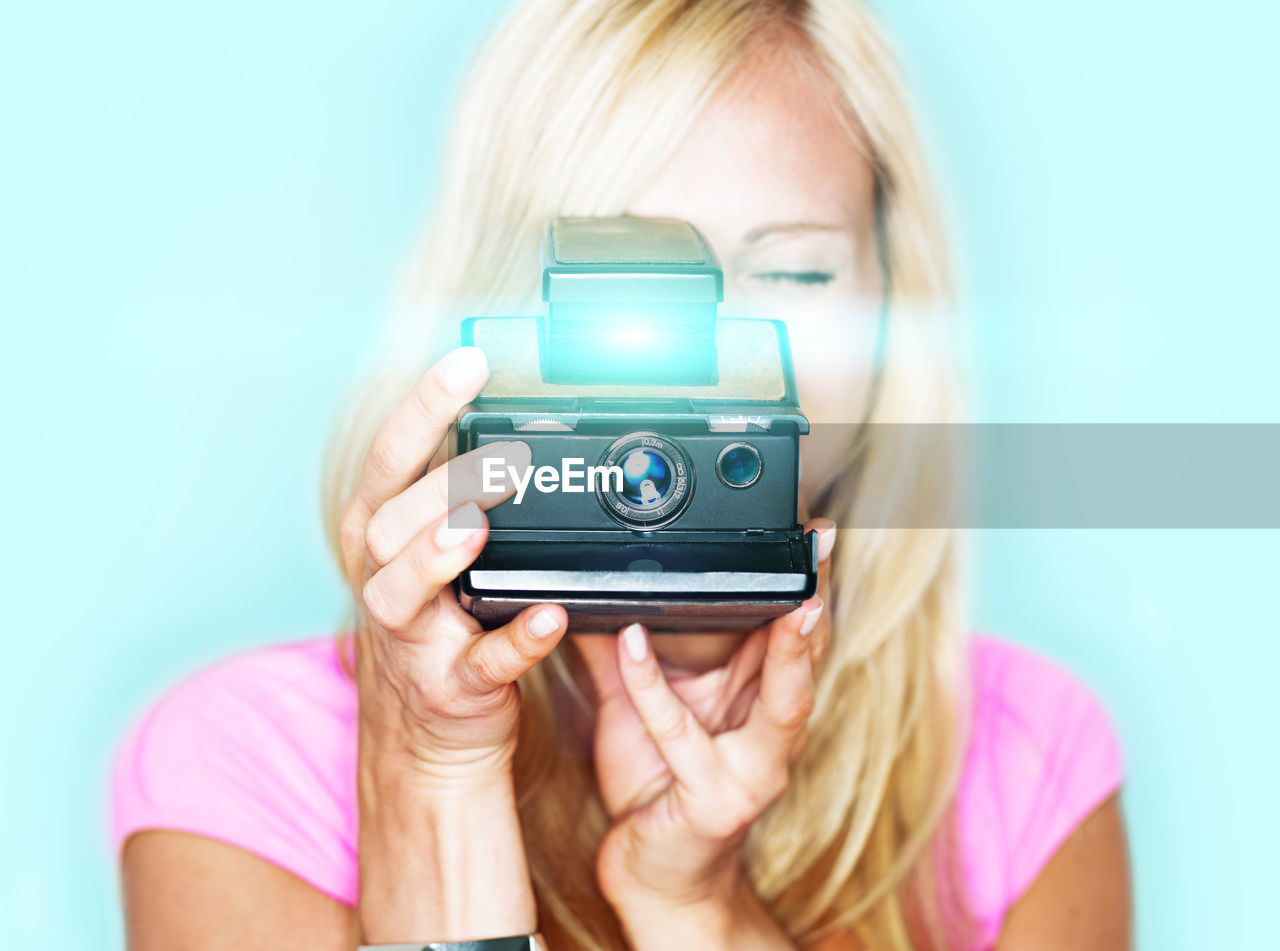 Woman photographing from polaroid camera against colored background
