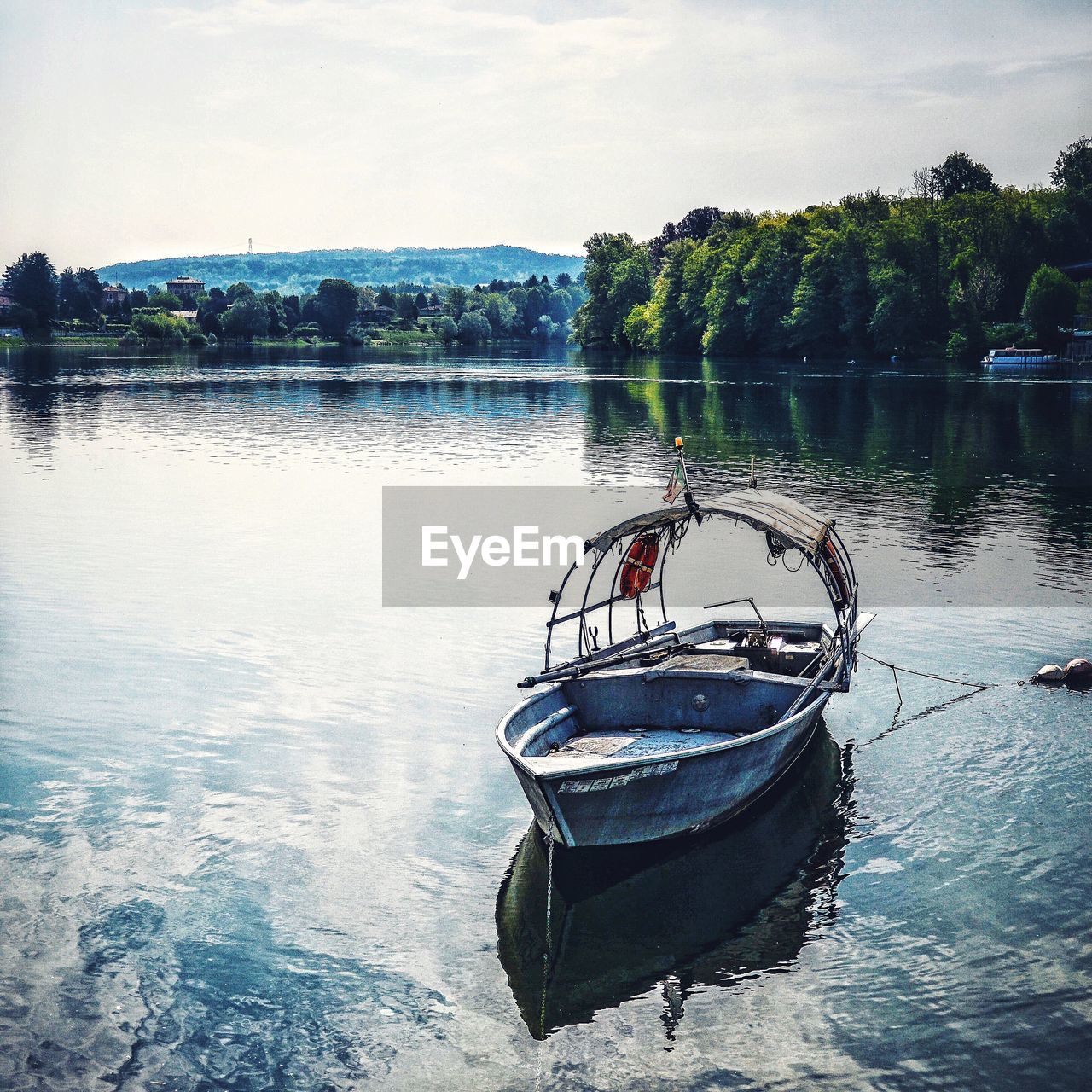 Boat moored on lake by trees against sky