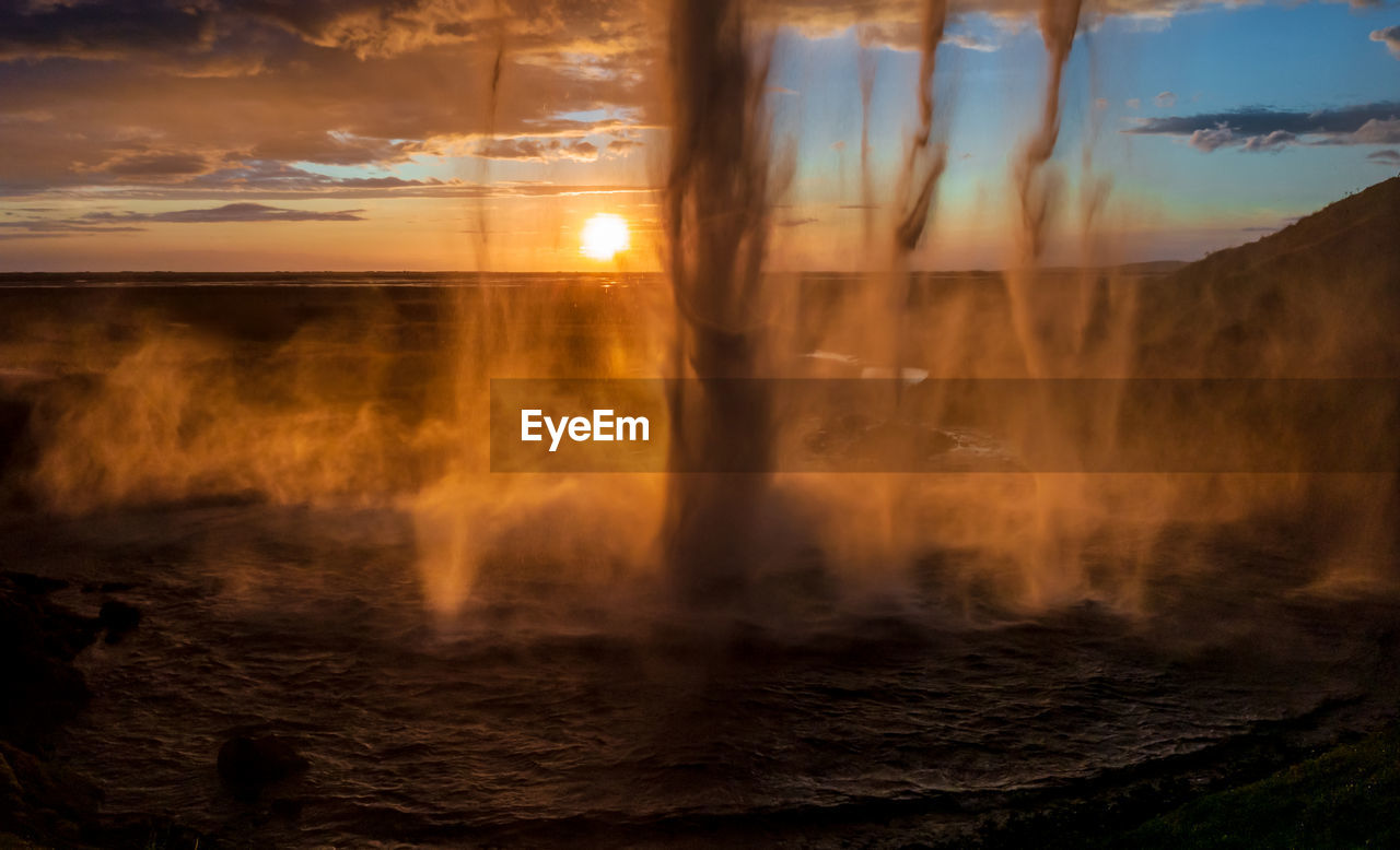 BLURRED MOTION OF TREES ON LAND AGAINST SKY AT SUNSET