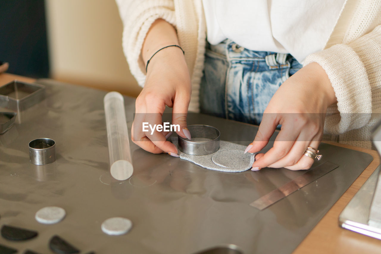 High angle of crop female designer cutting round pieces of fabric with metal form for handmade merch