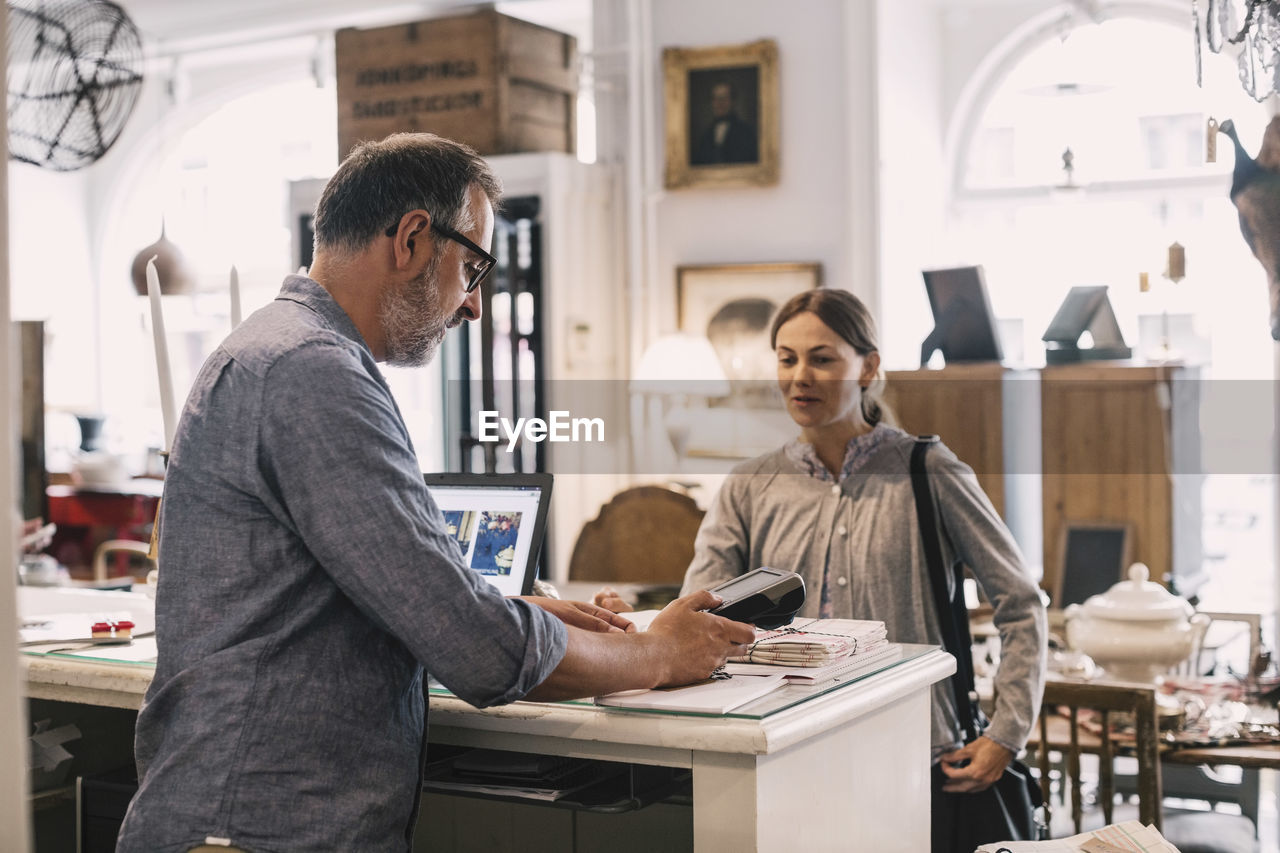 Owner using card reader in front of female customer at shop counter