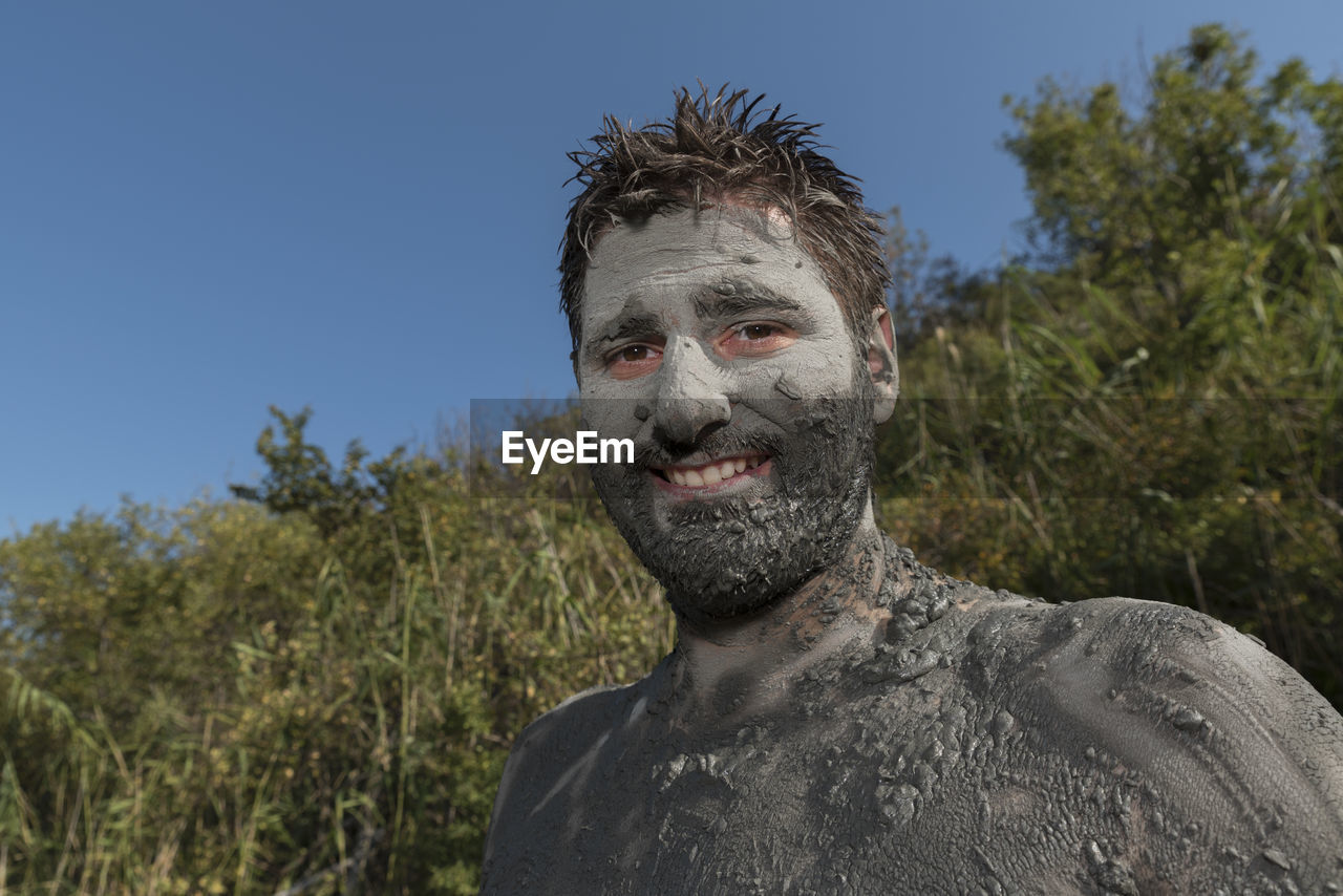 Portrait of man with mud on body against blue sky