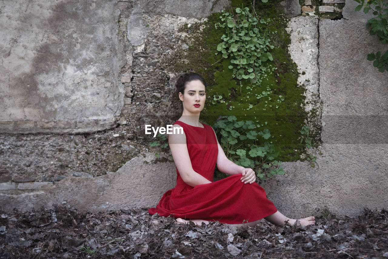 Portrait of young woman sitting by wall