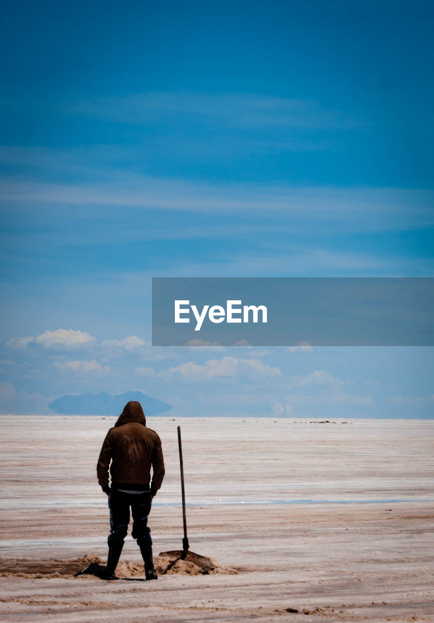 Rear view of hooded person standing on salt flat at salar de uyuni against sky