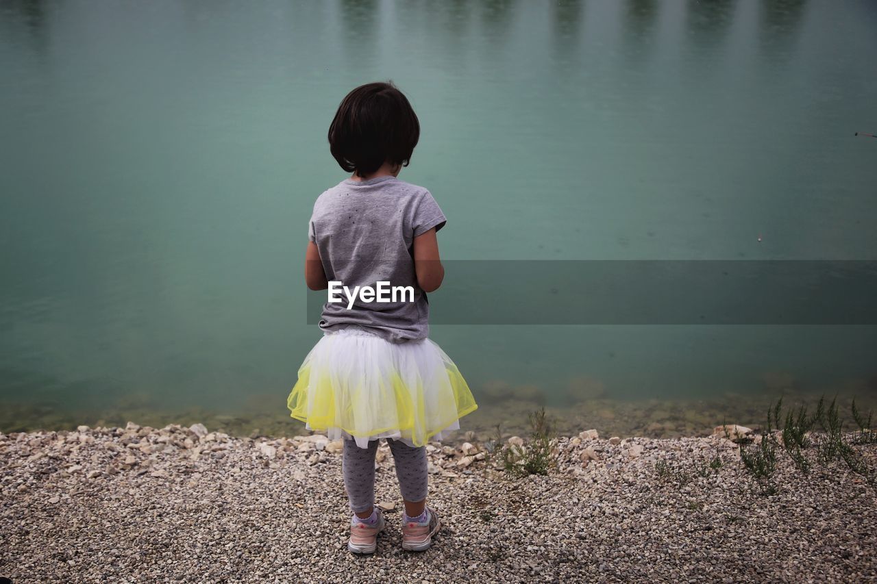 REAR VIEW OF WOMAN STANDING AT LAKE