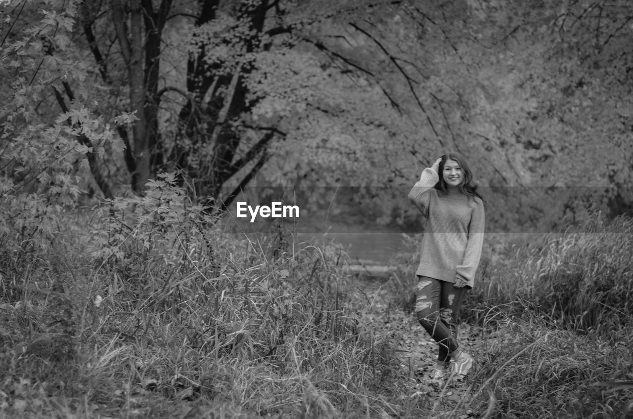 Portrait of beautiful girl standing amidst plants against tree