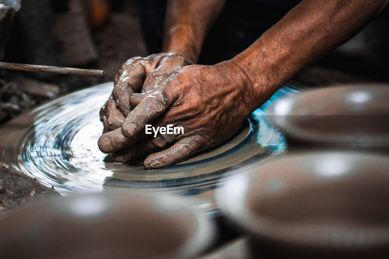 Cropped hands of person working with mud on pottery wheel