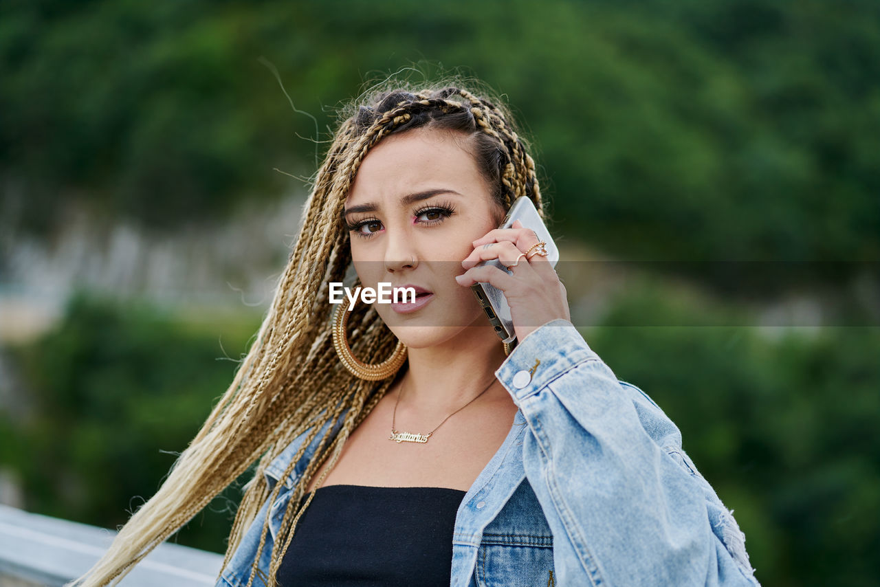 Close-up portrait of a young woman with braided blonde hair talking on her mobile phone