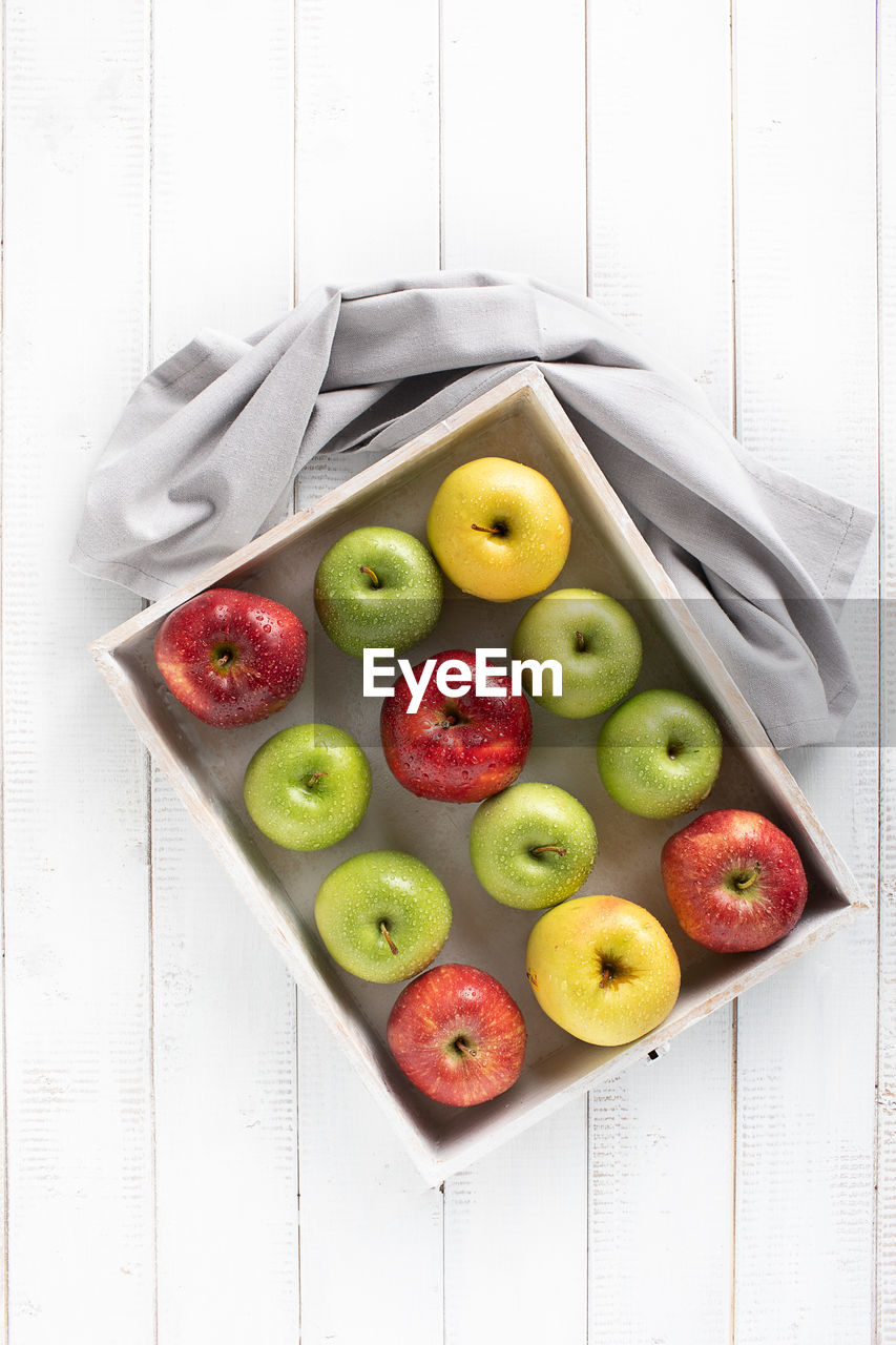 Colorful apples in a white wood tray on a white table top view
