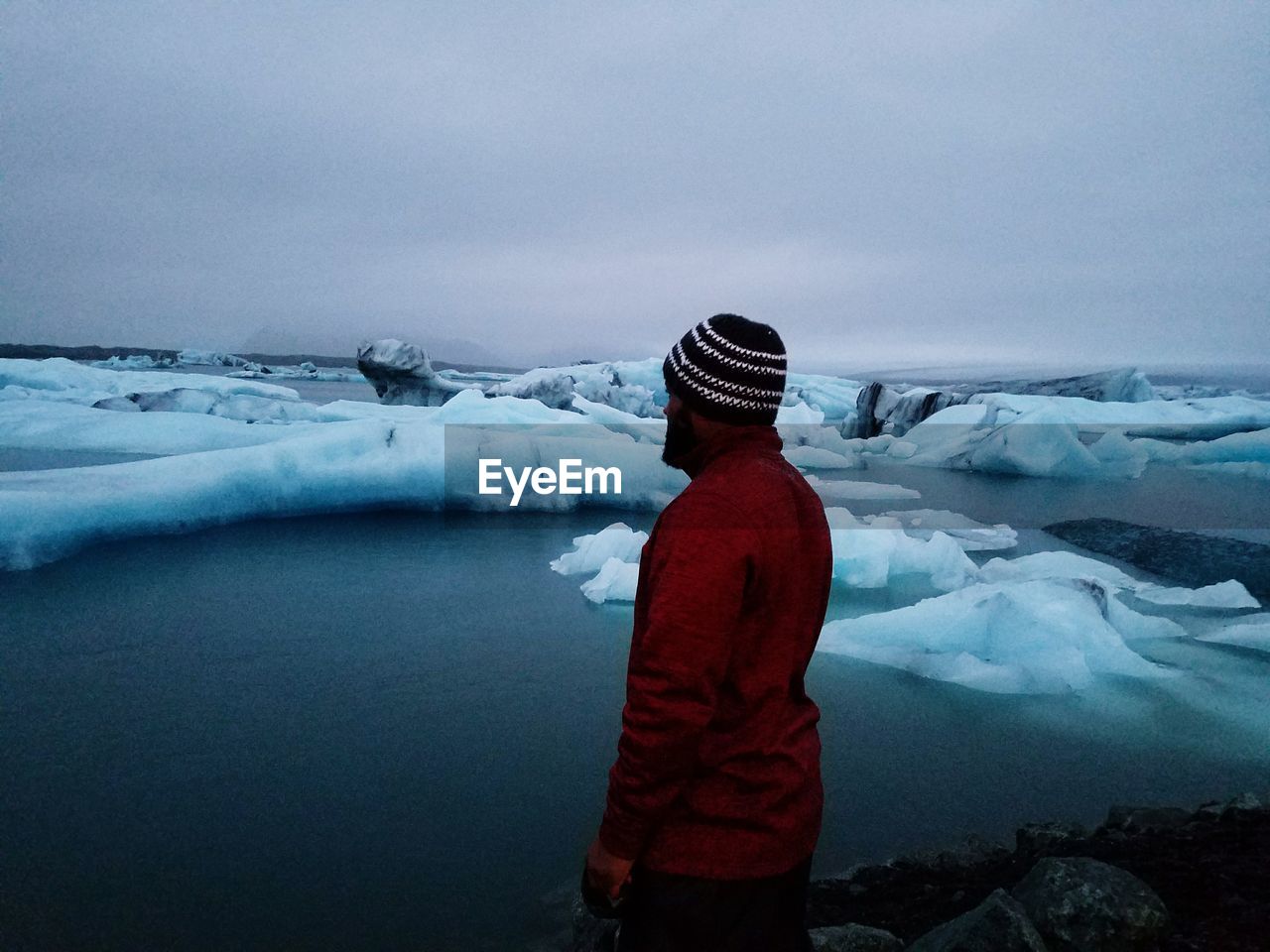 REAR VIEW OF MAN STANDING IN FROZEN LAKE