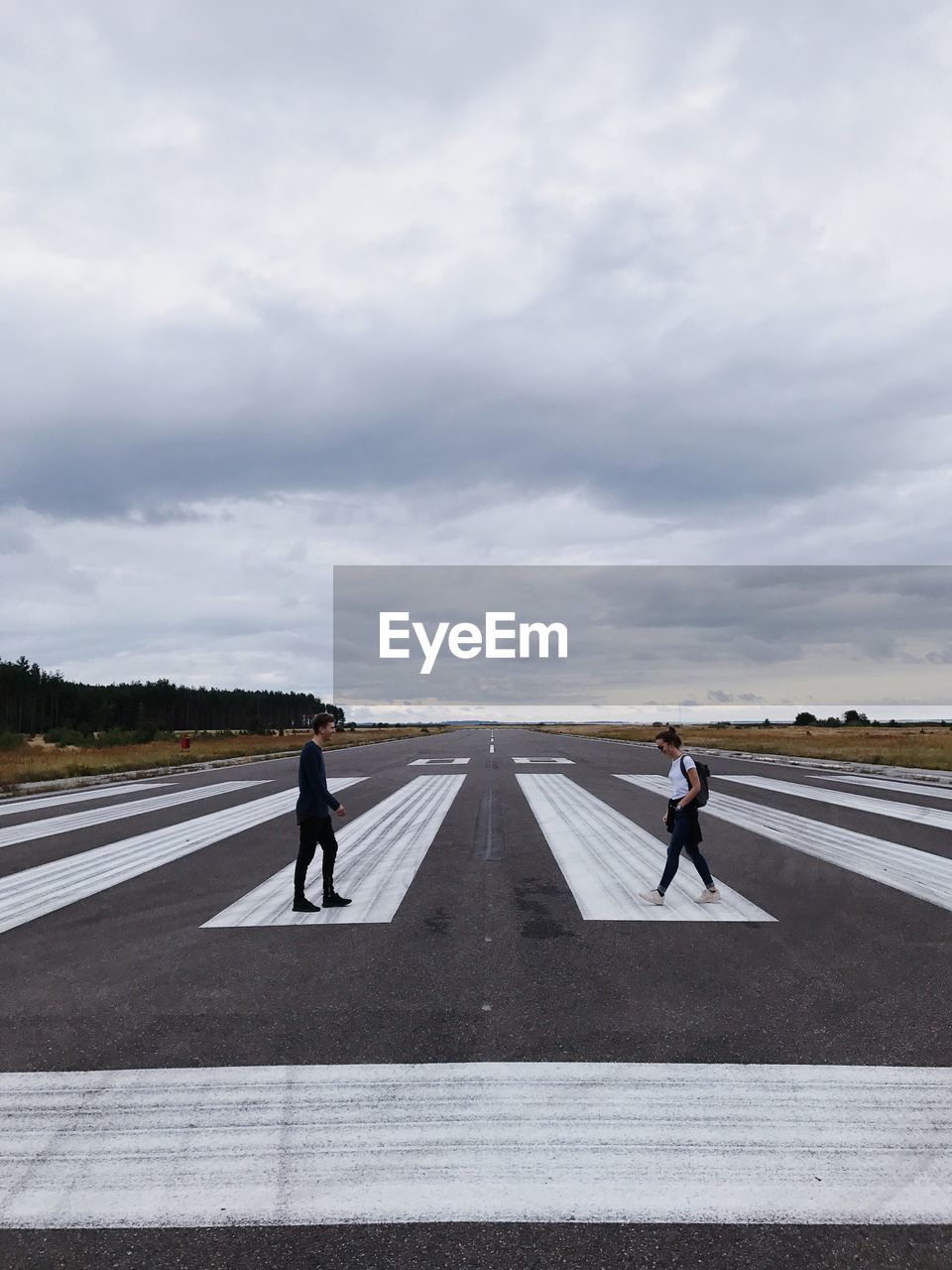 Friends walking on runway against cloudy sky