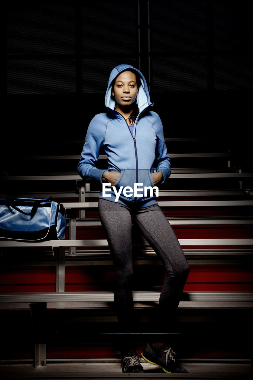 Confident sportswoman wearing hooded shirt standing with hands in pockets