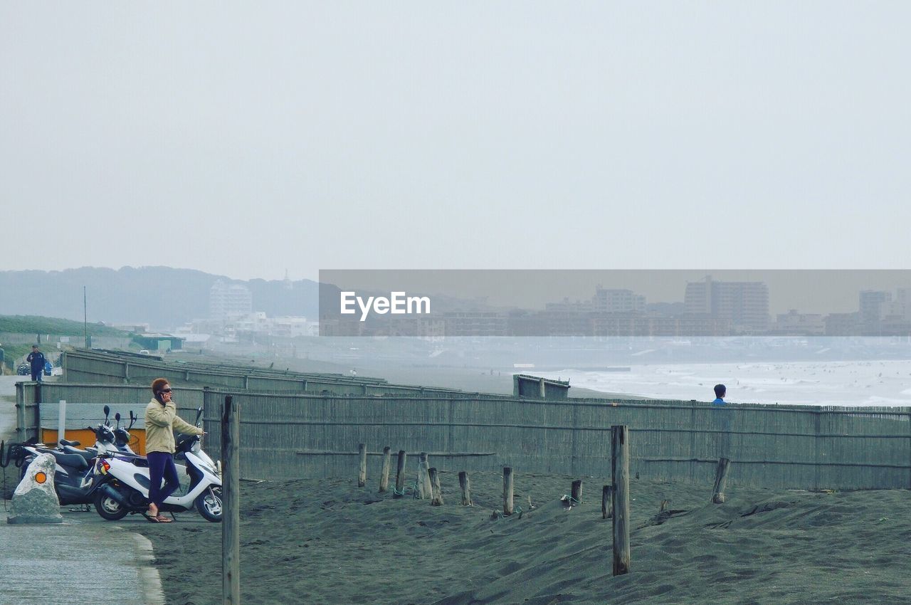 MAN SITTING AT BEACH AGAINST SKY