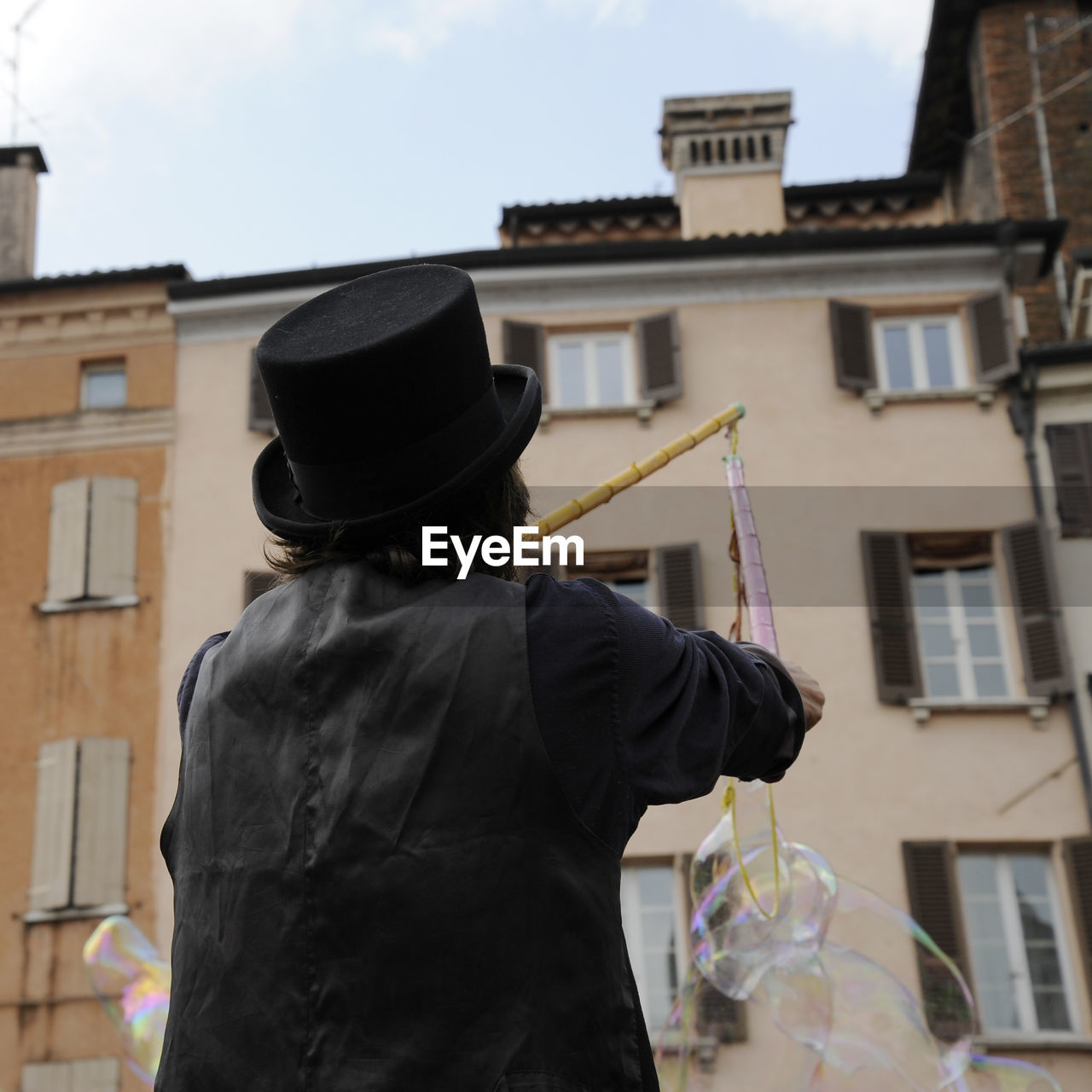 Rear view of man holding bubble wand against building