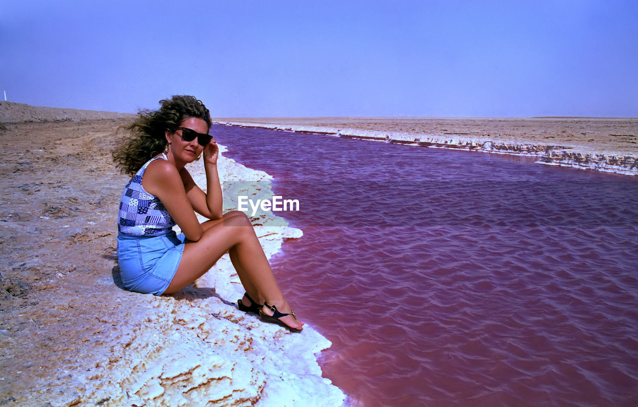 Young woman sitting on sunglasses against clear sky