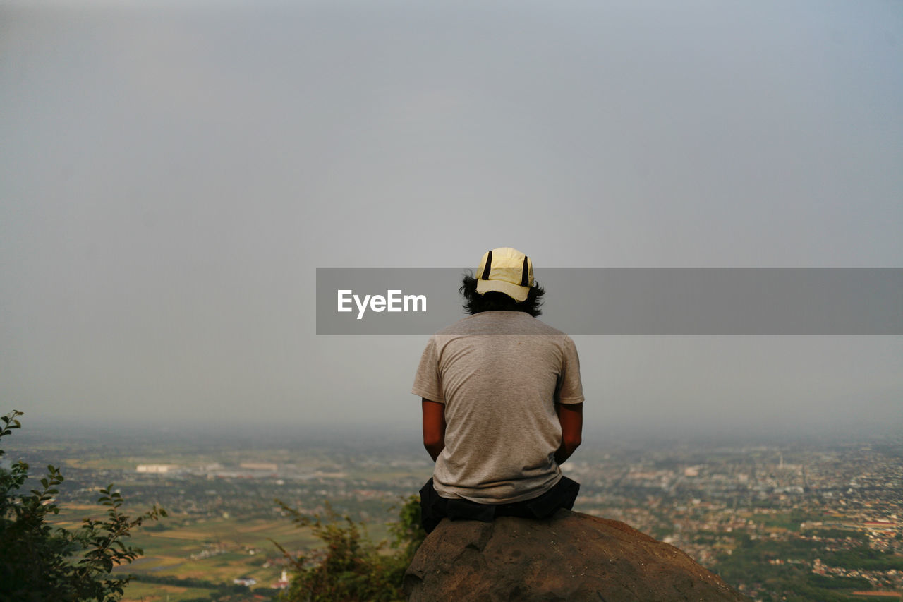 Rear view of man looking at cityscape against sky