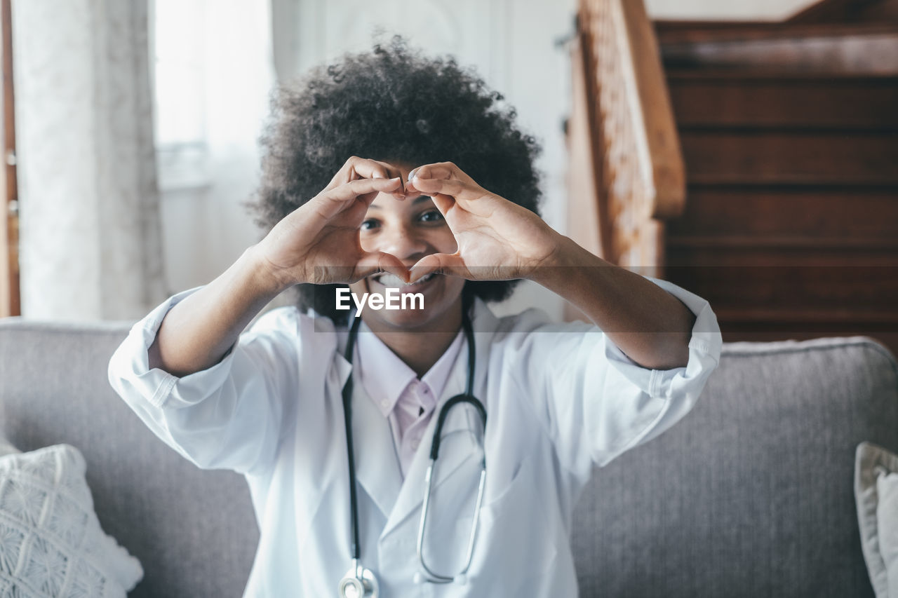 Portrait of doctor making heart shape sitting at home