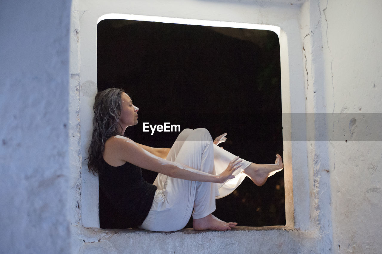 Woman covered with paint sitting on window sill at night