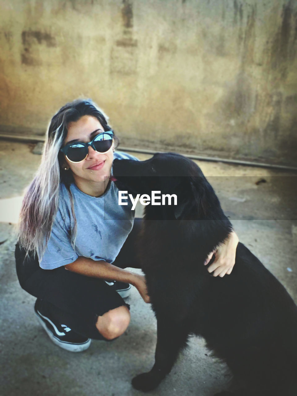 WOMAN WEARING SUNGLASSES SITTING WITH DOG ON CAMERA