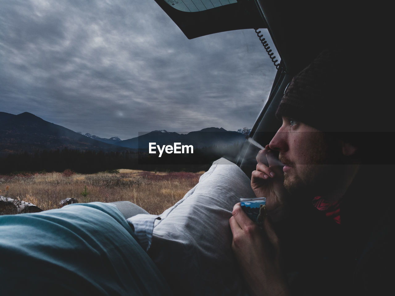 Close-up of man smoking cigarette in tent against cloudy sky