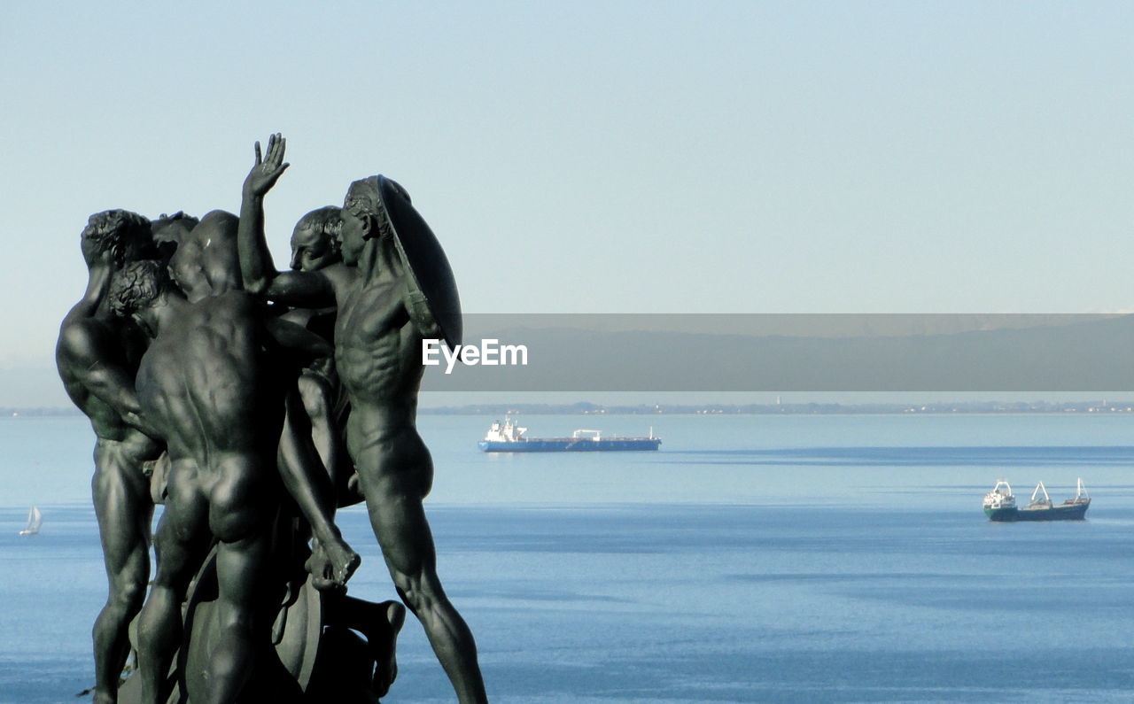 Human statues by sea against sky