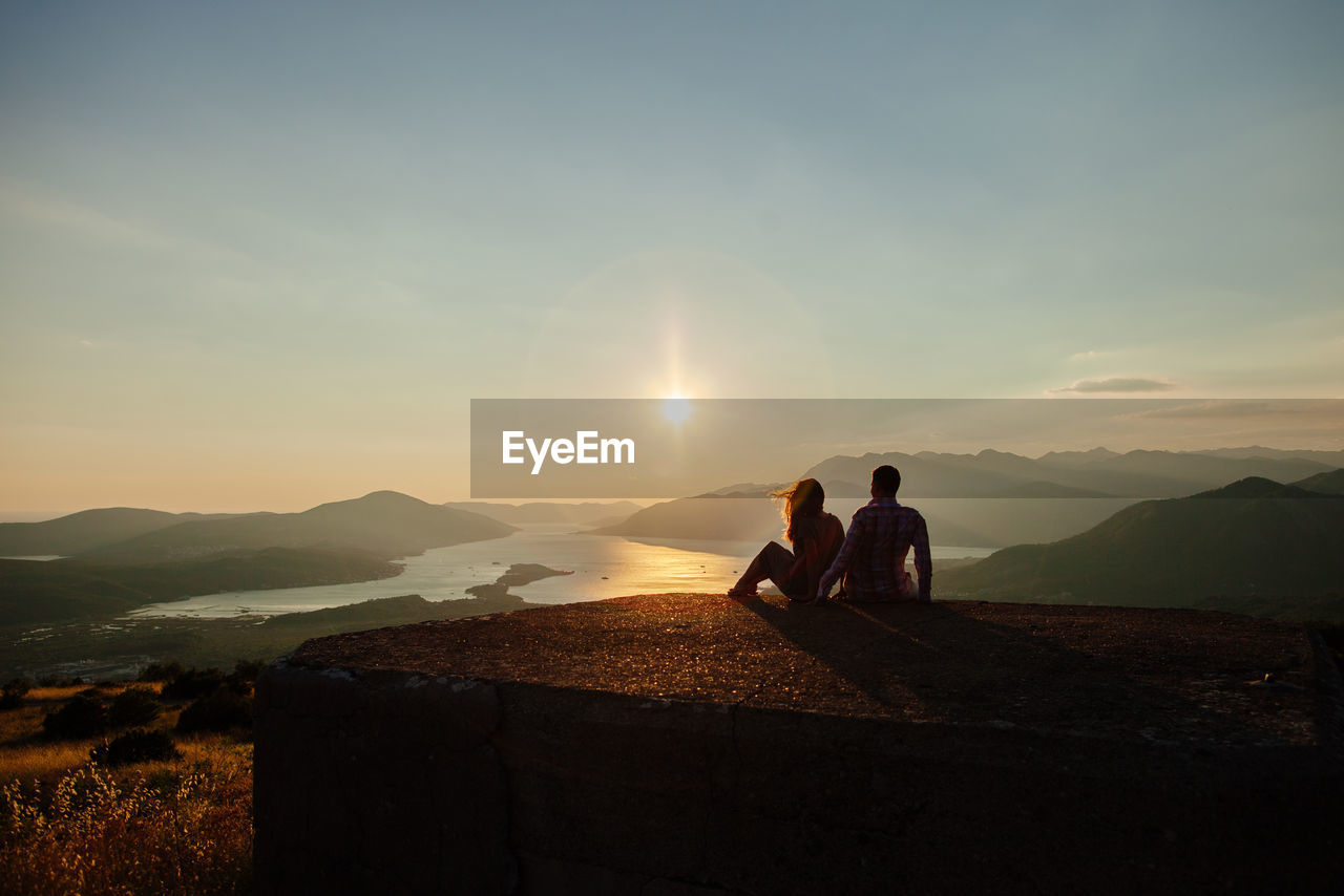 Couple on built structure against sky during sunset