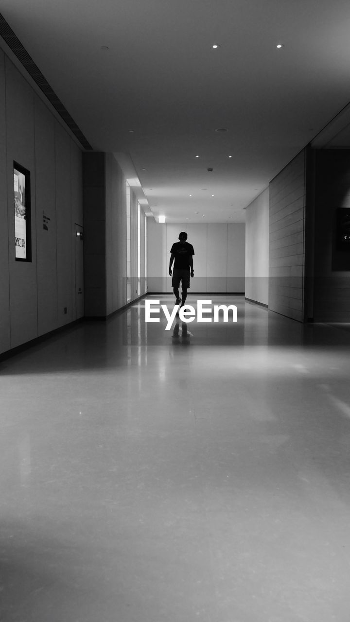 WOMAN WALKING IN CORRIDOR OF ILLUMINATED BUILDING