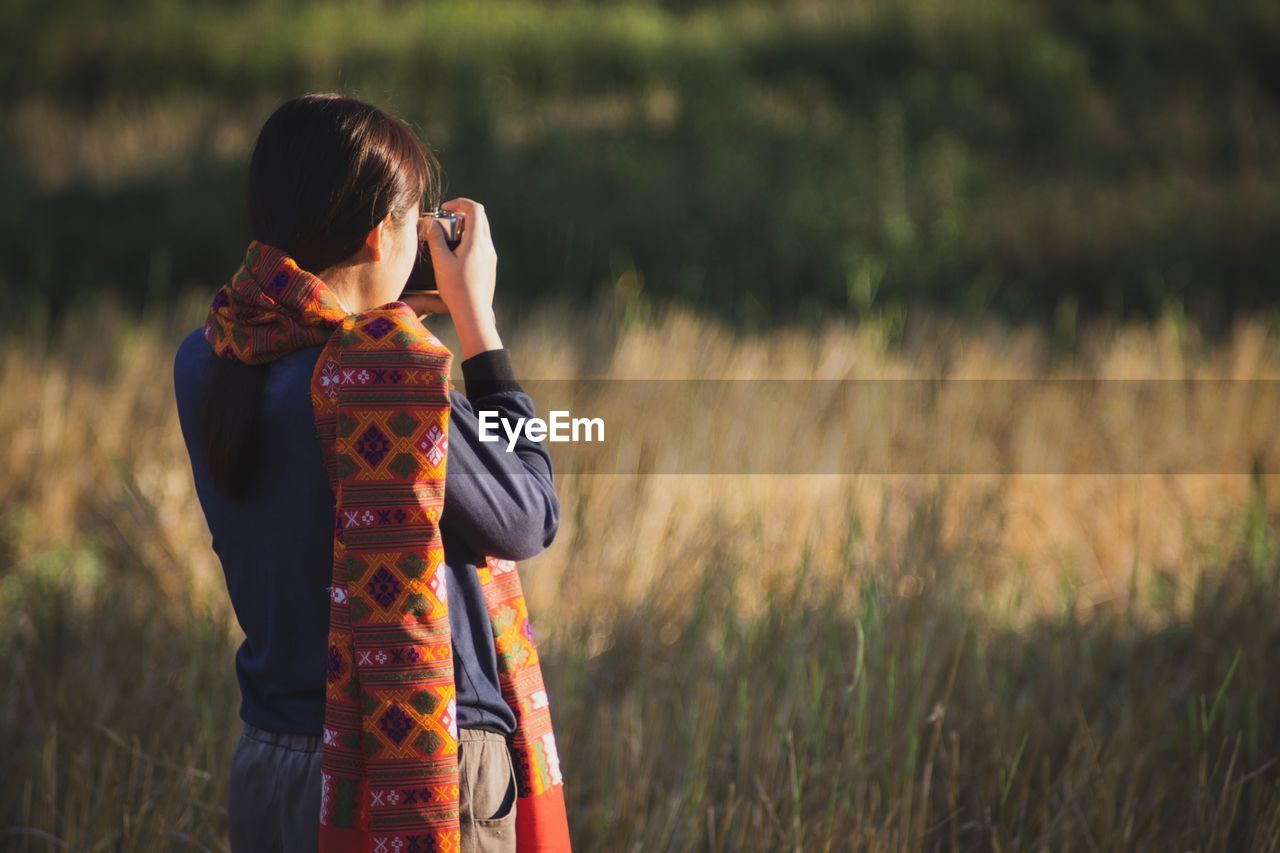 Rear view of woman photographing while standing on field