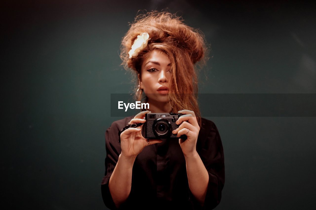 Portrait of young woman with camera against black background