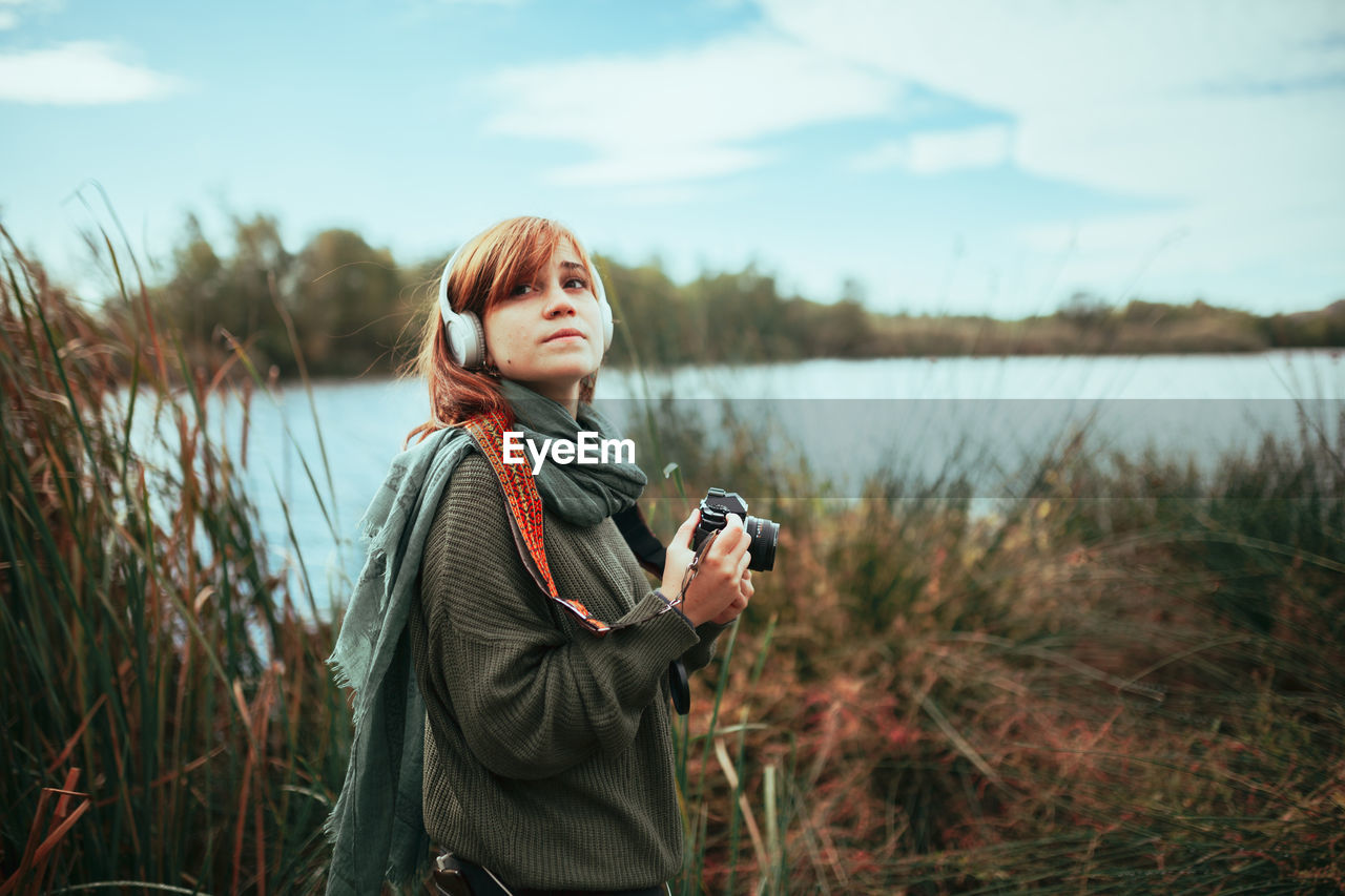 Young woman taking photos near to lake with an old analog camera