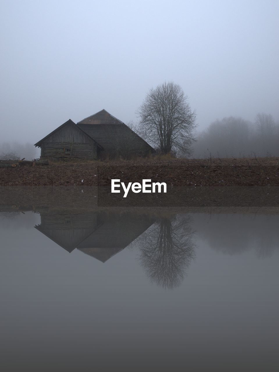 REFLECTION OF HOUSE ON LAKE BY TREE AGAINST SKY