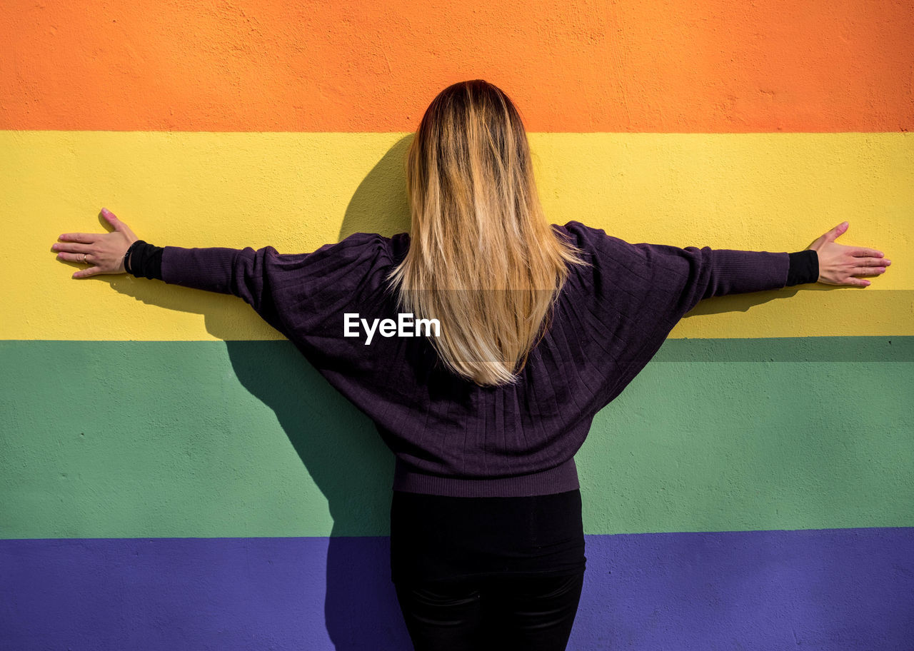 Rear view of woman with arms outstretched standing against colorful wall