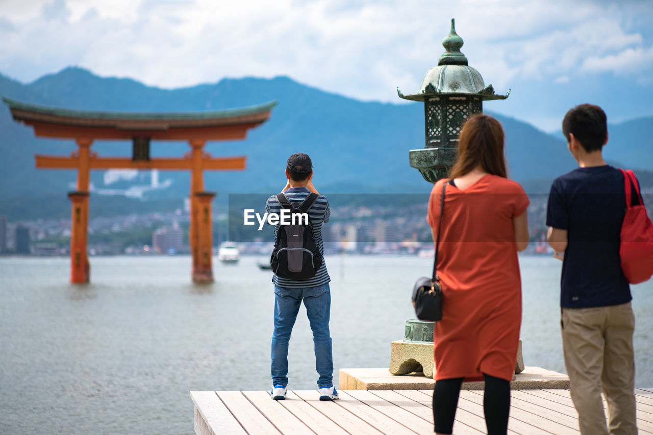 Rear view of people standing on pier by sea