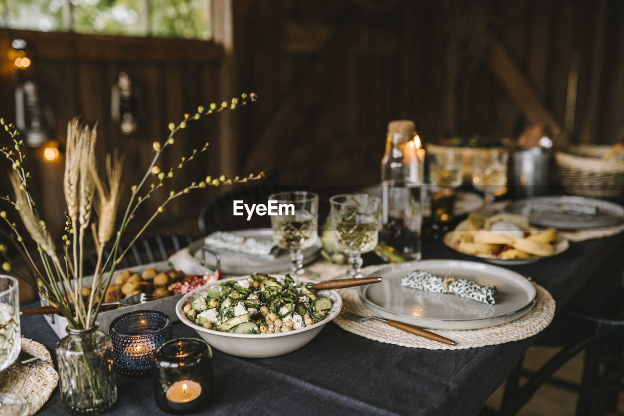 Food in bowl by plate and drinking glass arranged on dining table during social gathering